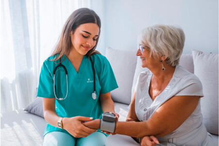 nurse in blue scrubs taking the pulse of a woman in her home