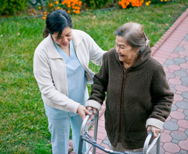 Nurse helping woman use walker outside