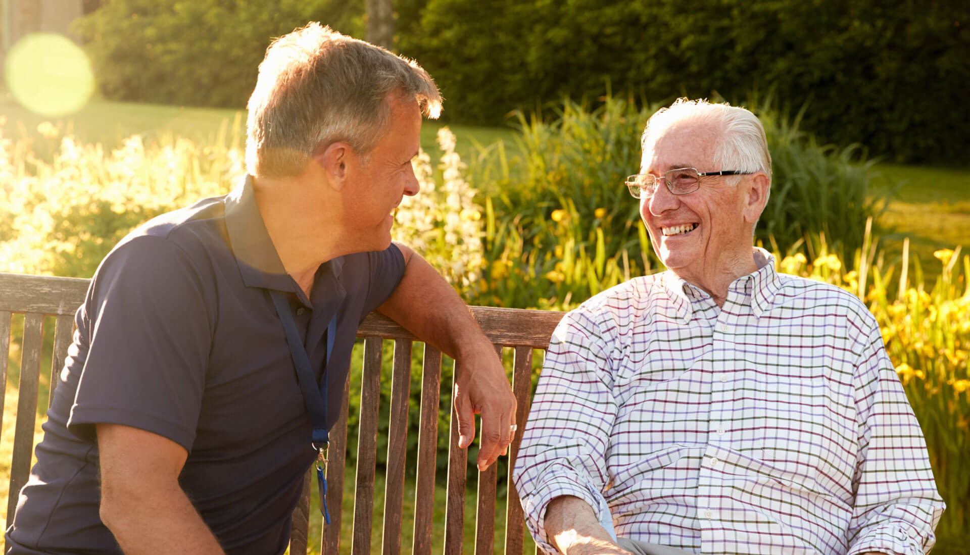 An older adult with his adult child spending time on a park bench.