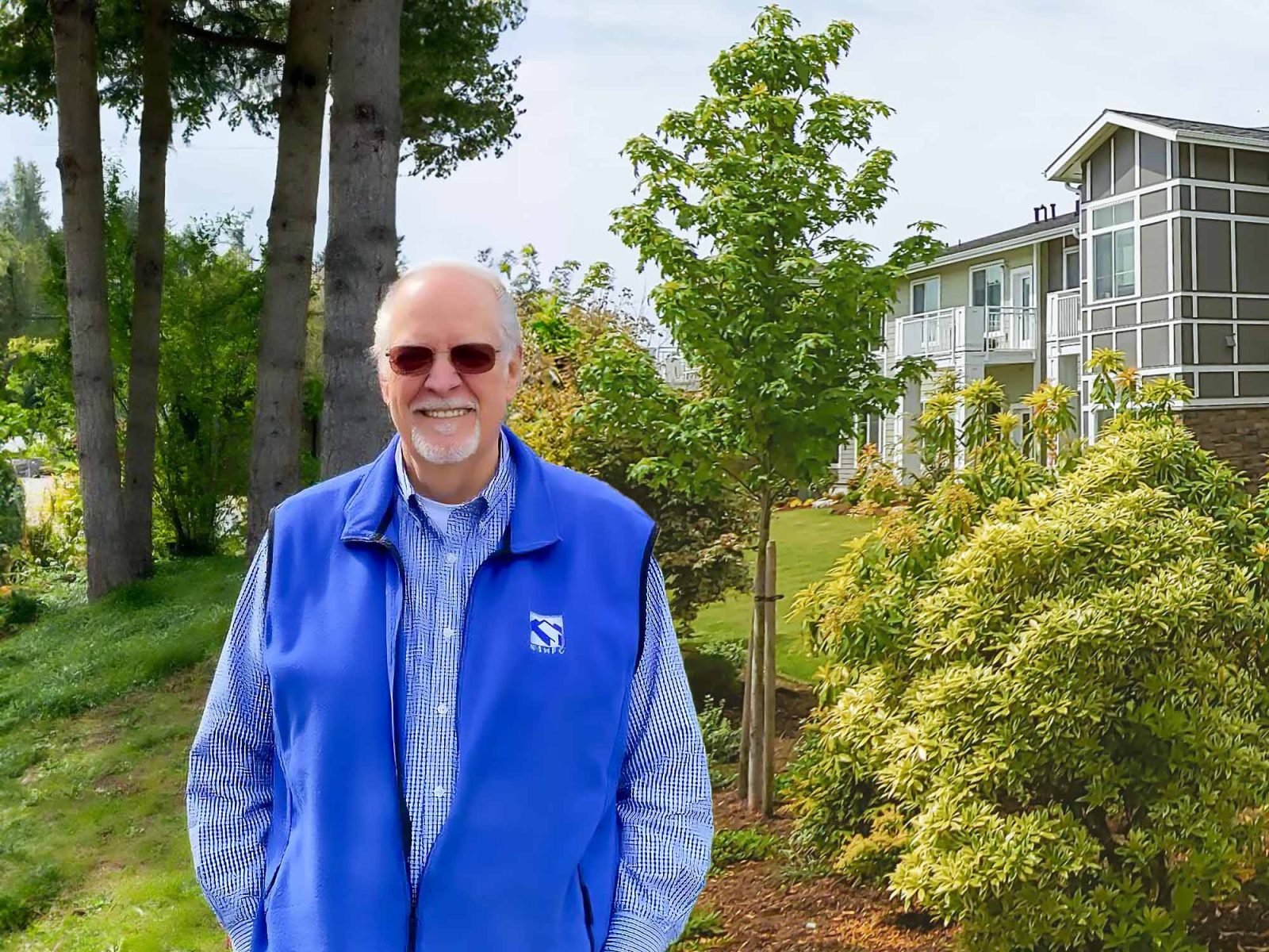 Happy man in bright blue vest smiling and standing in front of trees and wesley des moines building